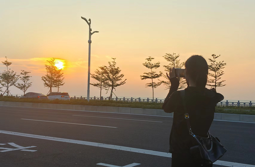 游客在廉州灣大道上拍落日